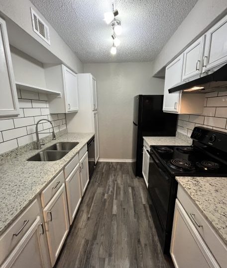 a kitchen with white cabinets and black appliances at The  Discovery Park Life Apartments